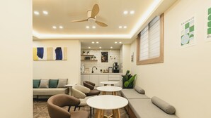 Um interior moderno com sofá, cadeiras e mesas, um ventilador de teto e uma cozinha ao fundo.
