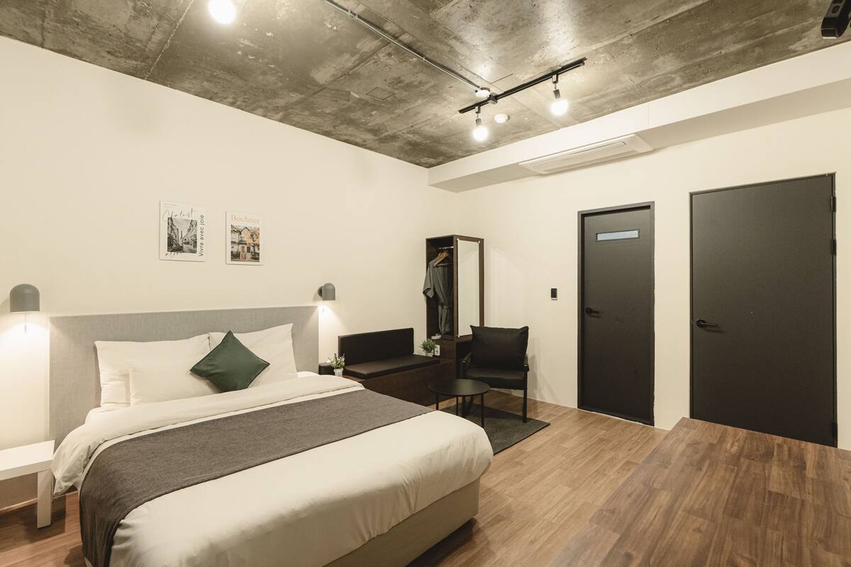 Ein modernes Hotelzimmer mit einem großen Bett, Nachttischen, einem Schreibtisch und einem Kleiderschrank.