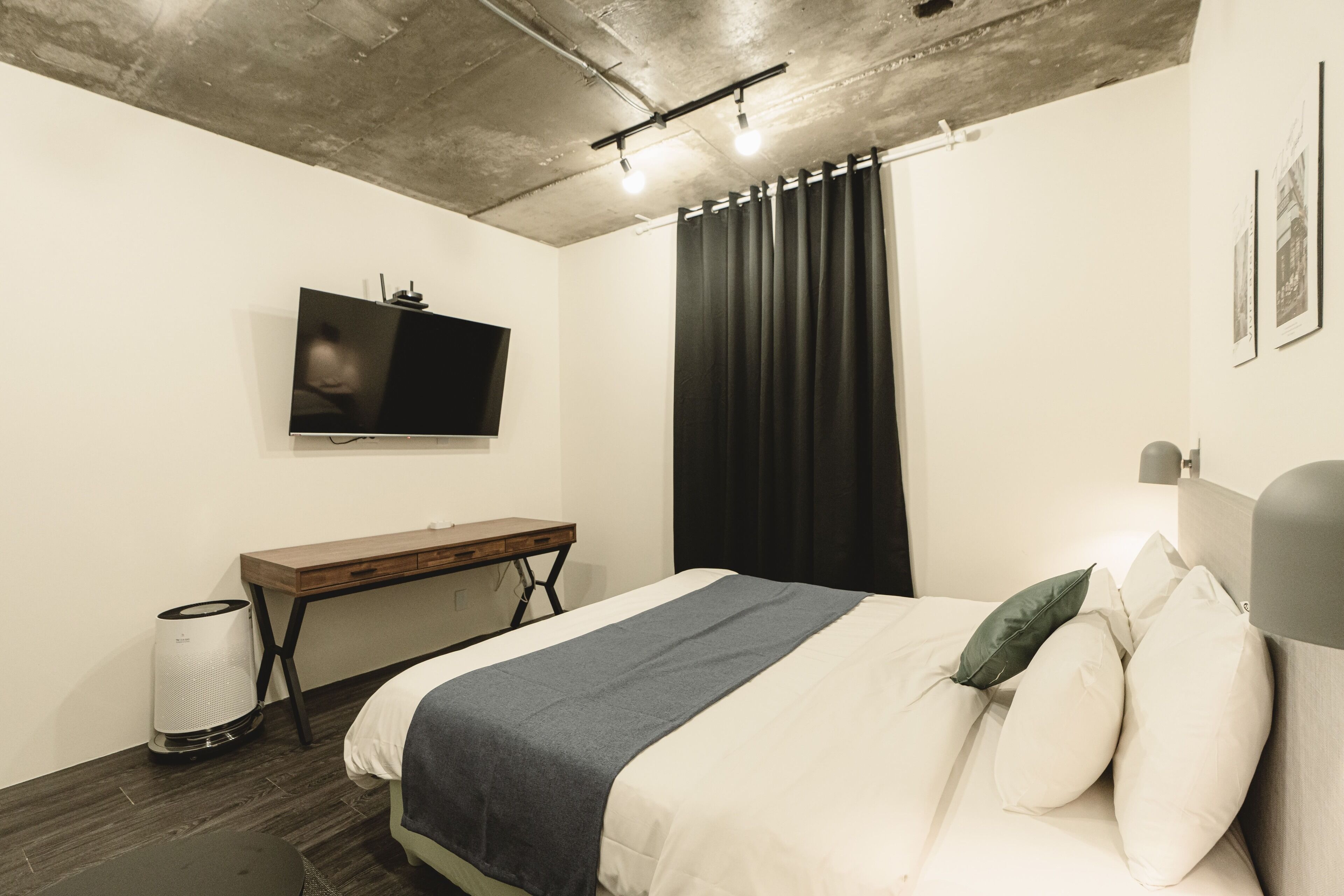 A modern bedroom with a bed, a desk, a TV, and a curtain.