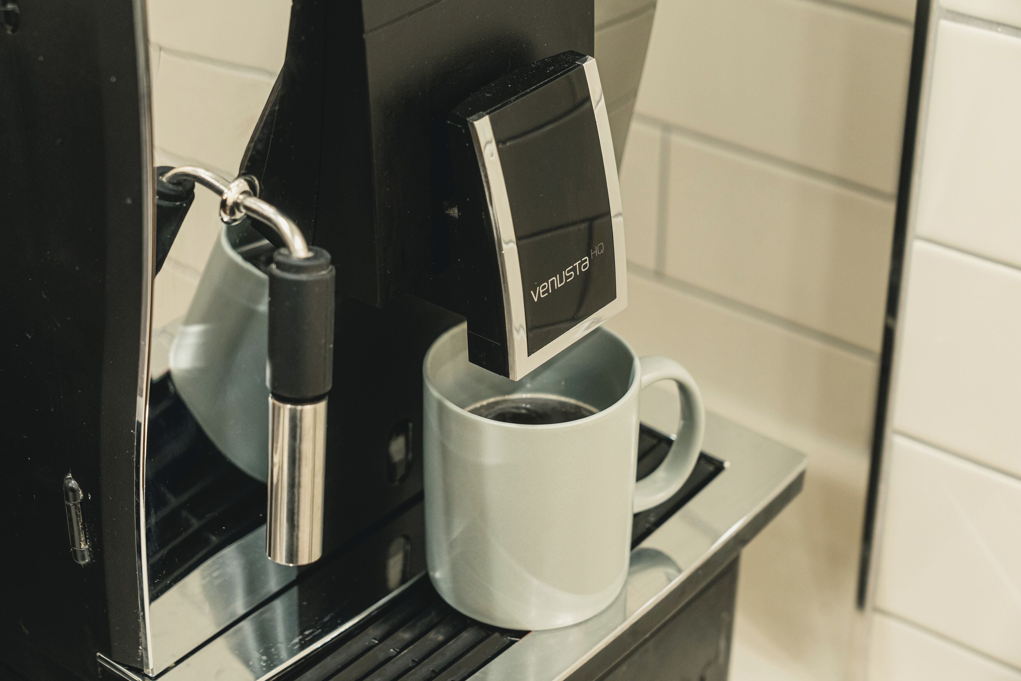 Una cafetera con pantalla digital, una taza de café y un asa metálico.