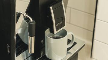 Una cafetera con pantalla digital, una taza de café y un asa metálico.