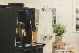 Una máquina de café con pantalla digital, dispensador de agua y una planta colgada en la pared.