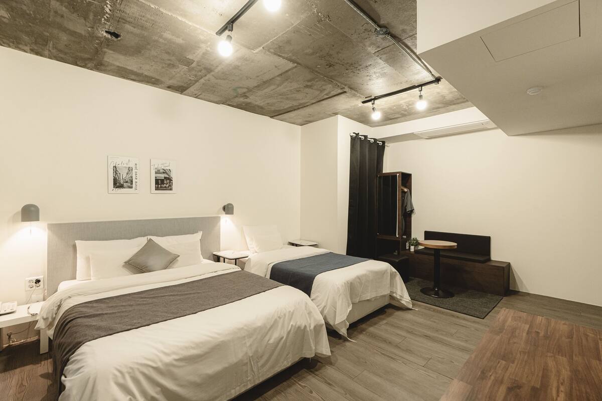 Ein modernes Hotelzimmer mit zwei Betten, einem kleinen Tisch und einem dunklen Vorhang.
