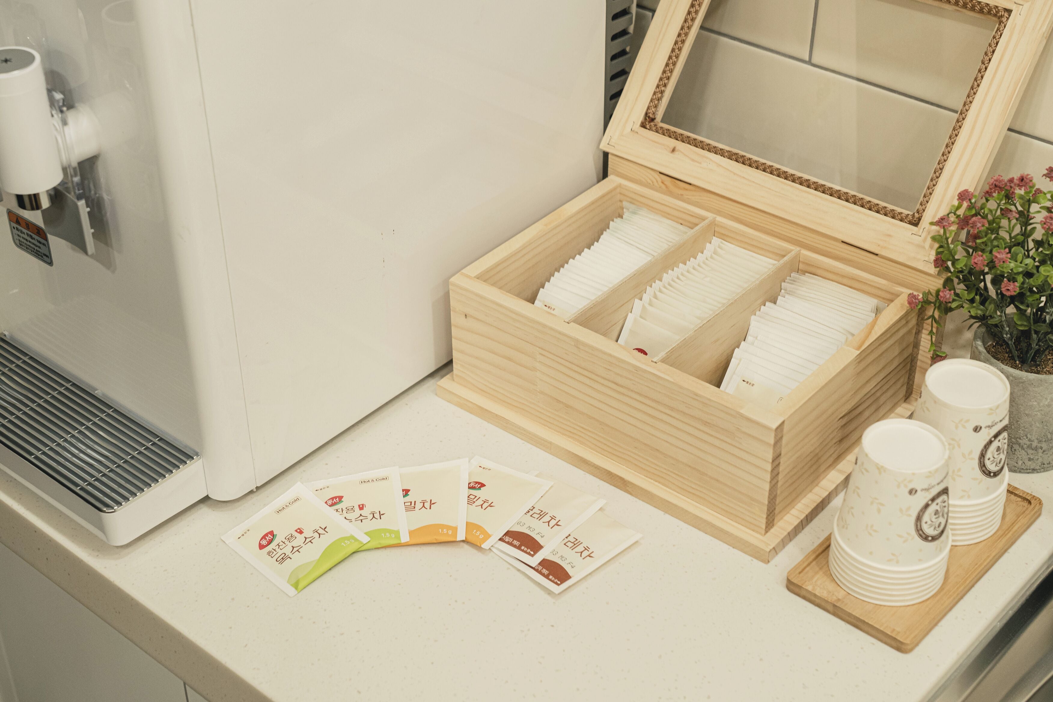 A wooden box with stacked white cups and saucers, a small potted plant, and a set of cards on a countertop.