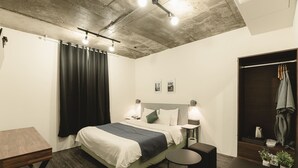 Quarto de hotel moderno com cama, mesas de cabeceira, uma pequena mesa redonda, guarda-roupa e área de chuveiro.