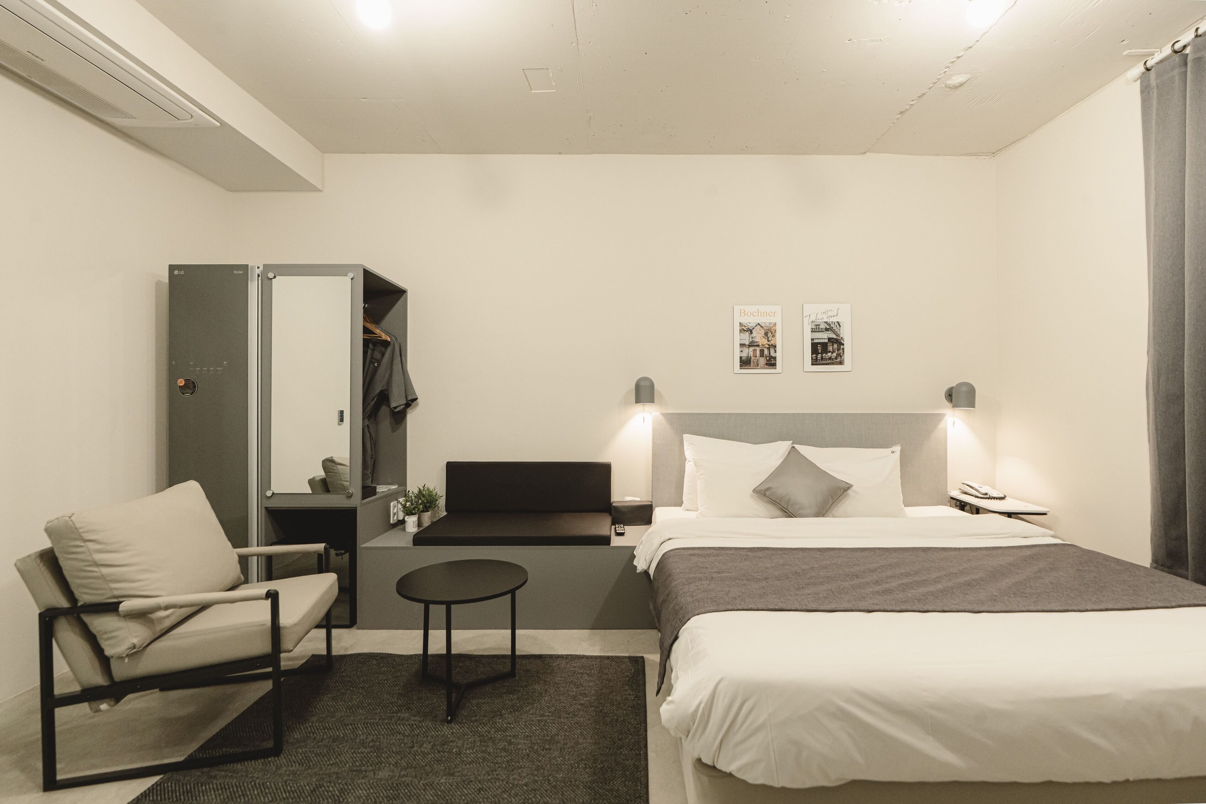 Habitación de hotel moderna con cama, una silla, una mesita, un espejo y una mesita de noche.