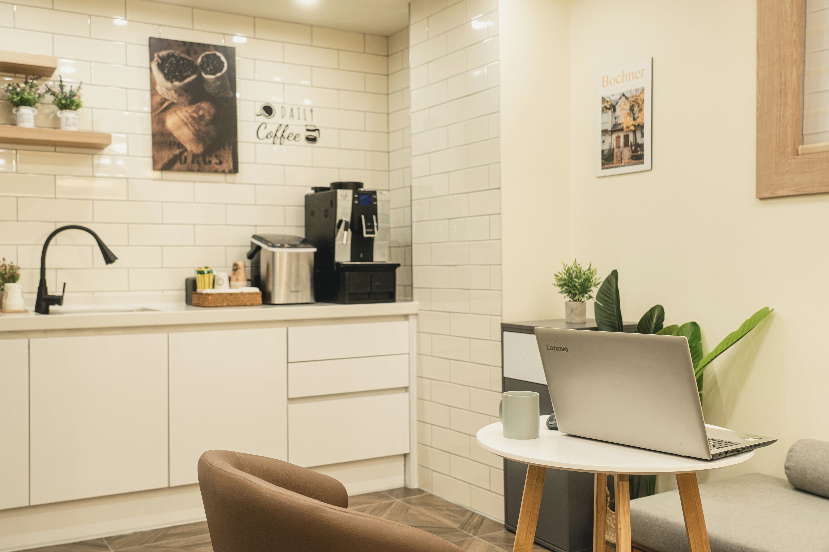 Eine moderne Küche mit weißen Schränken, einer Kaffeemaschine und einem Laptop auf einem kleinen Tisch.