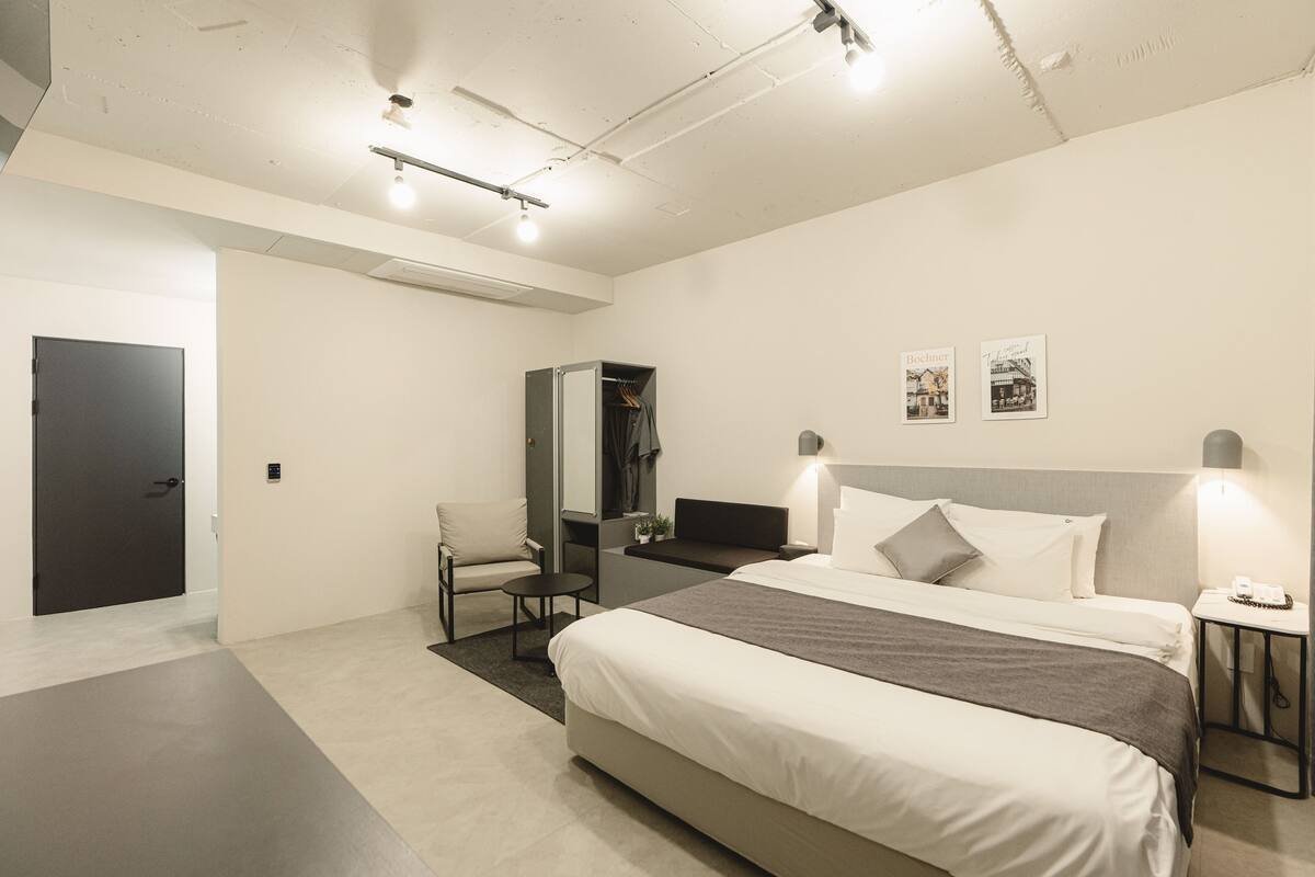 Ein modernes Hotelzimmer mit einem großen Bett, Nachttischen, einem Schreibtisch und einem Sessel.