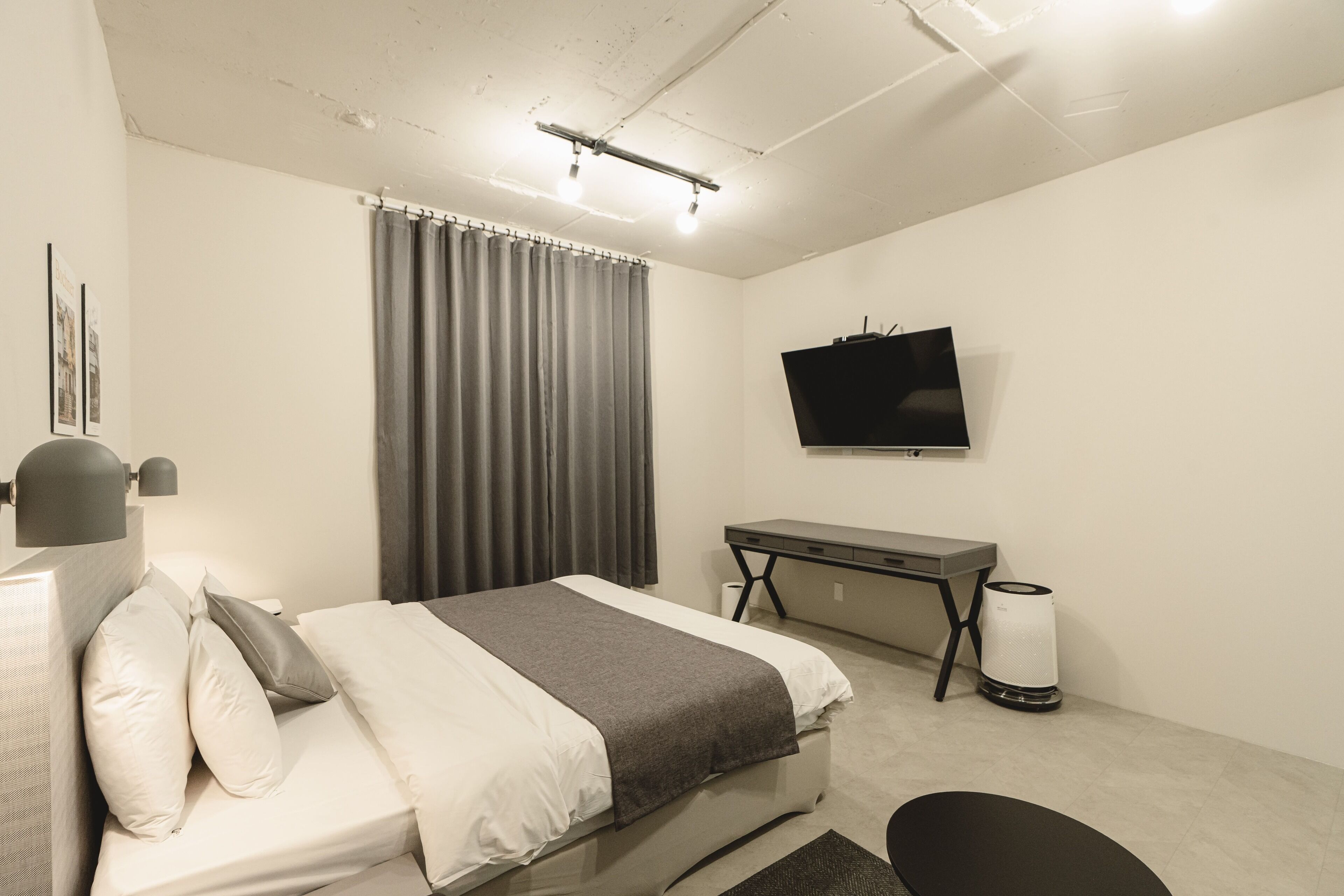 A modern bedroom with a bed, a desk, a television, and a waste bin.