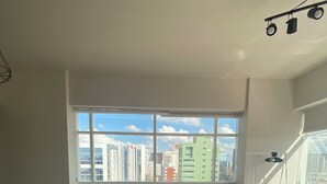 A modern, well-lit room with a large window, a bed, a desk with two stools, and a chair. - 2nd tallest building in Curitiba built (Curitiba)