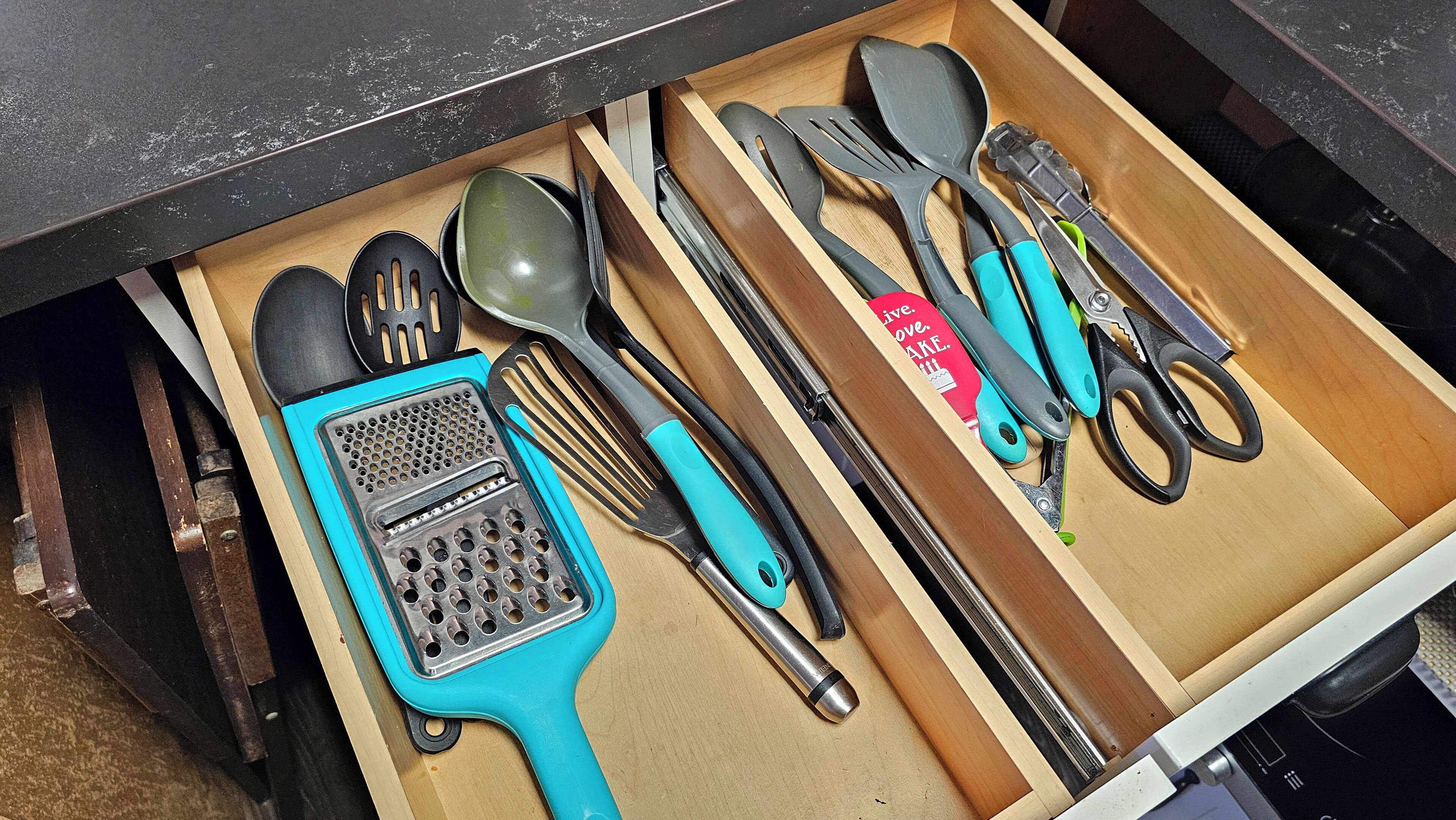 Un tiroir contenant divers ustensiles de cuisine, notamment une râpe, une spatule et des ciseaux.