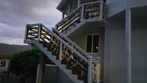 Una casa de dos pisos con una escalera adornada con luces, un balcón y vistas del paisaje circundante.