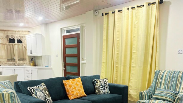 Una sala de estar con un sofá, dos sillones a rayas y una cortina amarilla.