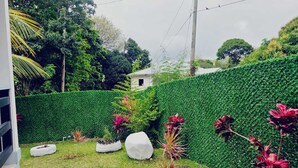 Un jardín bien cuidado con seto, una maceta blanca esférica y un pequeño árbol con flores rojas.
