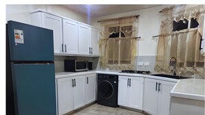 Una cocina compacta con armarios blancos, un refrigerador azul, un microondas, una lavadora y un lavamanos.