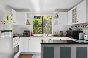 Eine moderne Küche mit weißen Schränken, einem großen Fenster und einer Kaffeemaschine.
