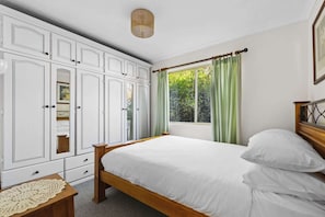 Ein Schlafzimmer mit Bett, Kleiderschrank, Fenster mit Vorhängen und Nachttisch.