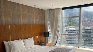 Camera d'albergo moderna con un letto grande, un comodino, una lampada e vista sulla città attraverso ampie finestre.