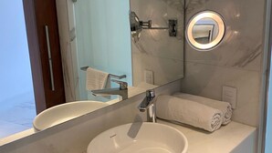 Un bagno moderno con una parete in marmo, uno specchio rotondo con illuminazione, un lavabo bianco e un appendi-asciugamani.