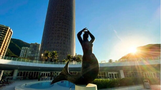 Una scultura di una sirena in una piazza pubblica, con un alto edificio sullo sfondo.