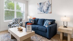 A modern living room with a blue sofa, patterned armchair, and a coffee table with decorative items. - Elegant Stay • Downtown • Steps to Convention Ctr (Hot Springs)
