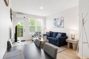 Ein modernes Wohnzimmer mit einem dunkelblauen Sofa, einem Esstisch und einem Fernseher.