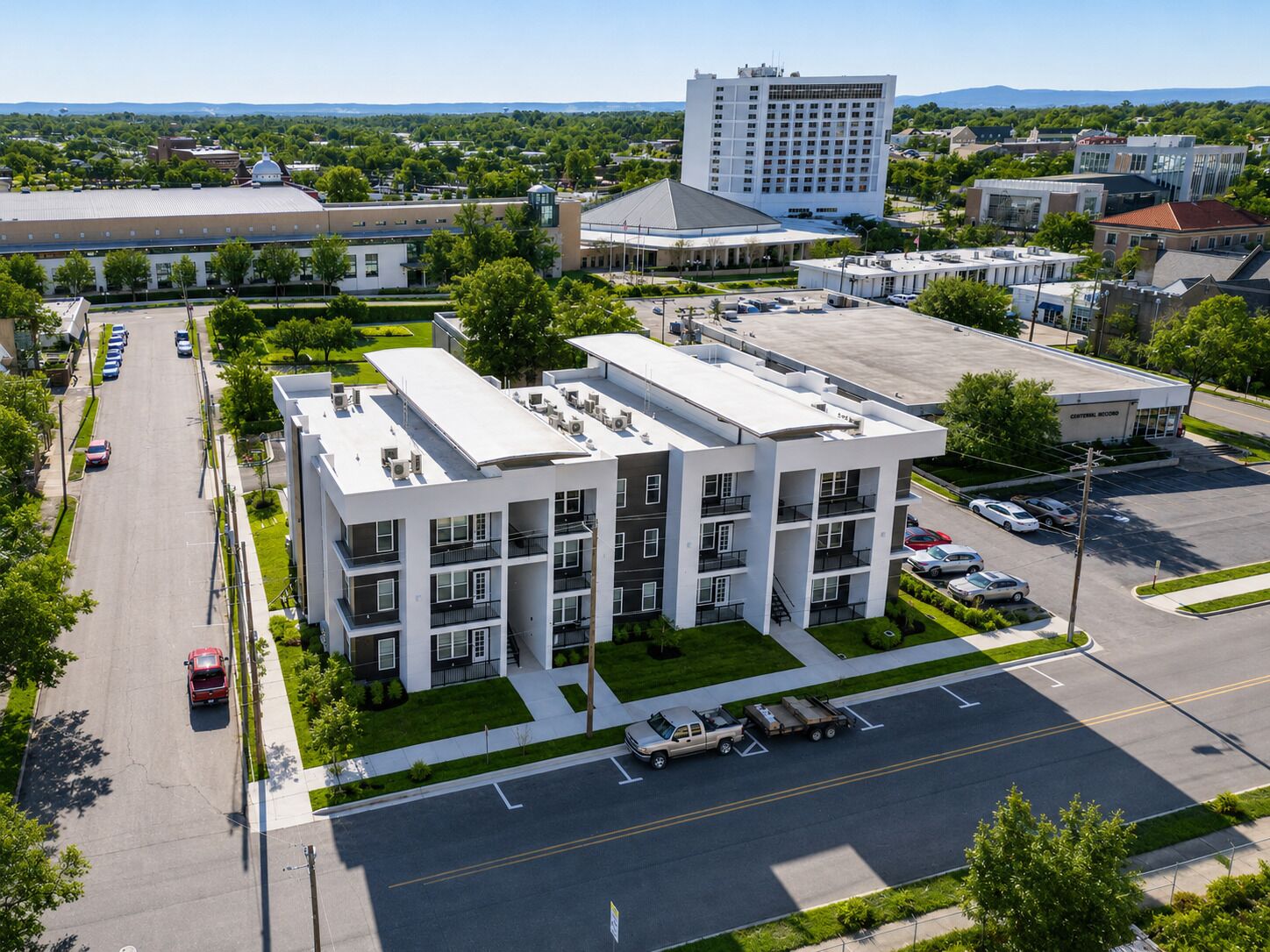 A multi-story building with a flat roof, parking lot, and surrounding greenery.