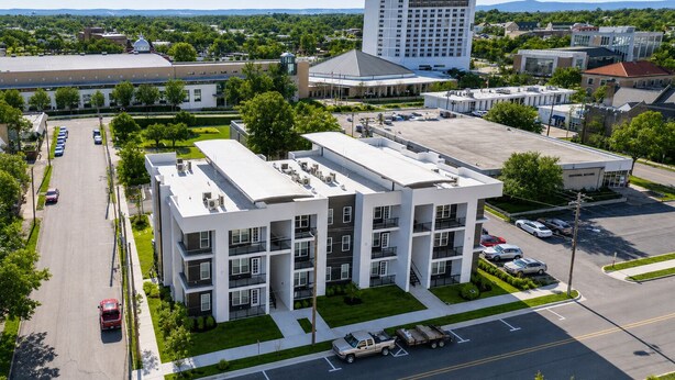 A multi-story building with a flat roof, parking lot, and surrounding greenery. - Elegant Stay • Downtown • Steps to Convention Ctr (Hot Springs)