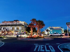 A street intersection with a roundabout, palm trees, and buildings with signage. - 2 Bed Condo w/pool right on Bradenton Beach! Walk to Everything! (Bradenton Beach)