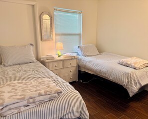 Ein Hotelzimmer mit zwei Betten, einem Nachttisch, einer Lampe und einem Fenster mit Jalousien.