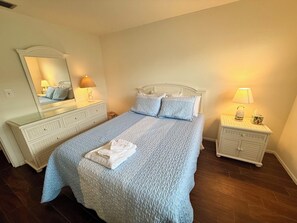 A bedroom with a large bed, two bedside tables, a dresser, and a mirror. - 2 Bed Condo w/pool right on Bradenton Beach! Walk to Everything! (Bradenton Beach)