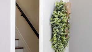 A white door with a green plant decoration and a black doorbell.