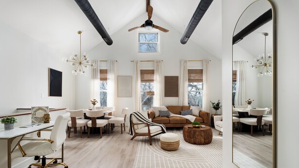 A spacious living room with a high ceiling, a ceiling fan, a large mirror, and a dining area with a round wooden table and chairs.