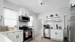 A modern kitchen with white cabinetry, a stainless steel stove, and a microwave. There are wooden shelves above the stove and a refrigerator on the right.