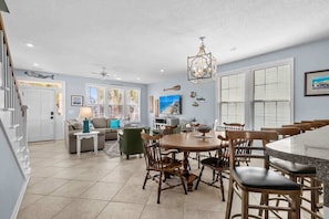 A spacious living area with a dining table, chairs, and a kitchen area. - About Time: Surfside Beach House (Surfside Beach)