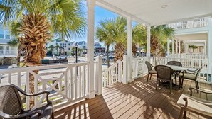 A covered outdoor area with wooden flooring, white railings, and several chairs and tables. - Ocean View Surfside House w/ Pool & Walk to Bars (Surfside Beach)