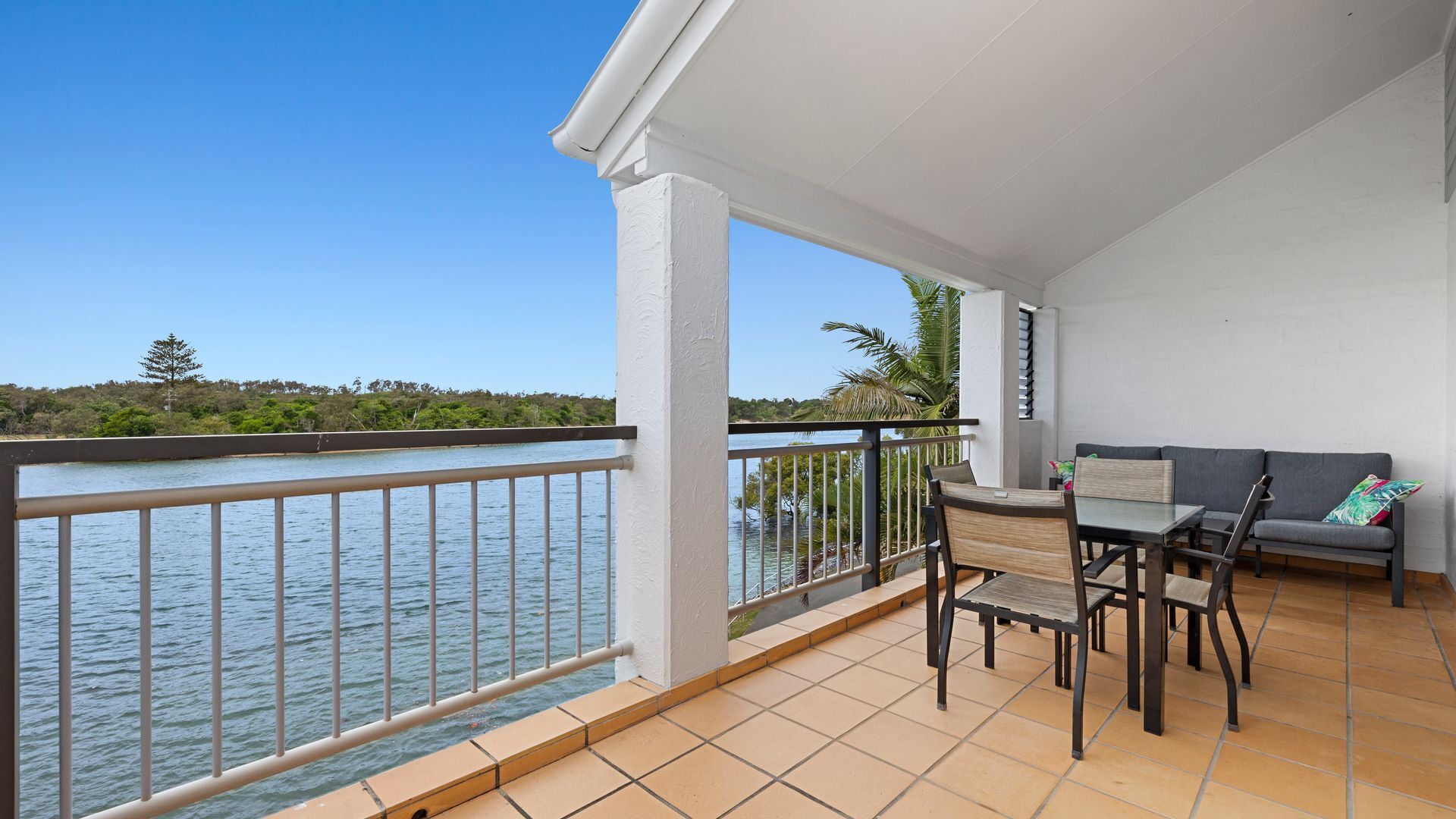 A balcony with a view of the water, a table with chairs, and a sofa.