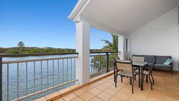 A balcony with a view of the water, a table with chairs, and a sofa.