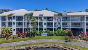 Ein mehrstöckiges Hotel mit Balkonen, einem Schild mit der Aufschrift "Sunrise Cove" und einer angelegten Fläche mit tropischen Pflanzen.