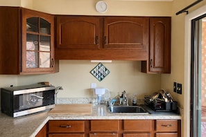 Une cuisine avec des meubles de rangement en bois, un four à micro-ondes, un évier et une horloge au mur.