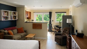 Une pièce bien éclairée, avec un lit, un canapé, une petite table, une chaise, un téléviseur et une bibliothèque.