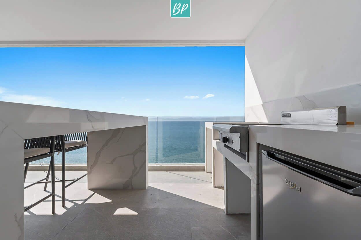 A modern kitchen with a view of the ocean, a seating area with a table and chairs, and a sign indicating the location.