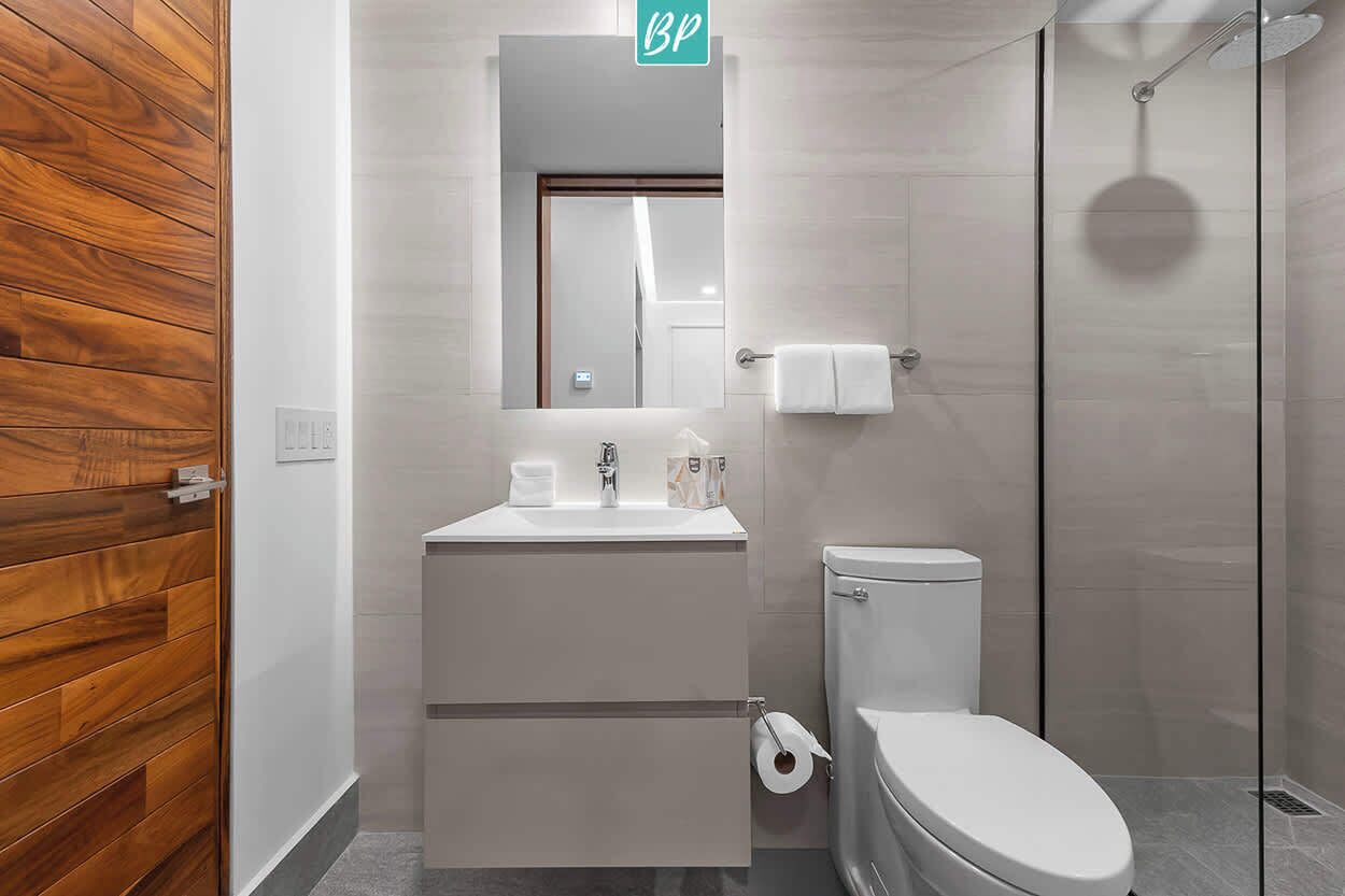 Un baño moderno con pared de paneles de madera, un lavabo blanco con espejo arriba, un inodoro y una ducha con mampara de vidrio.