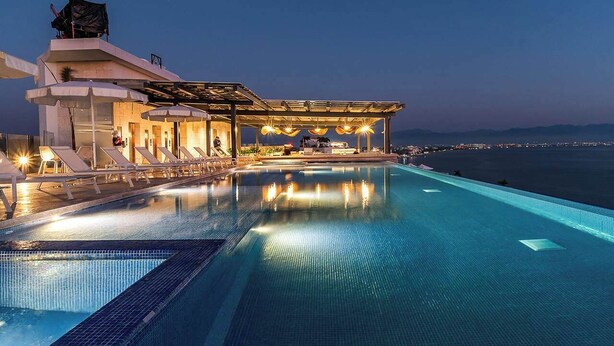 A modern infinity pool with a view of the sea, a covered outdoor seating area, and a building with a rooftop terrace. - 4BR Hidden Gem: Luxe Oceanfront Living in Bucerias (Bucerías)