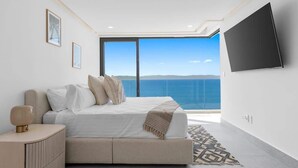 A modern bedroom with a large bed, a nightstand, a TV mounted on the wall, and a view of the sea. - 4BR Hidden Gem: Luxe Oceanfront Living in Bucerias (Bucerías)