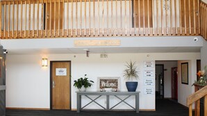 A reception area with a wooden sign above the door, a welcome sign, a potted plant, and directional signs for guest services.