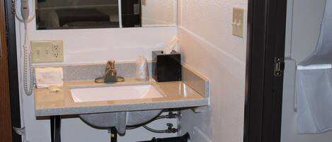 A bathroom with a sink, mirror, towel dispenser, and a hairdryer on the wall.