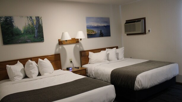 A hotel room with two beds, a nightstand, a wall-mounted air conditioner, and two paintings.