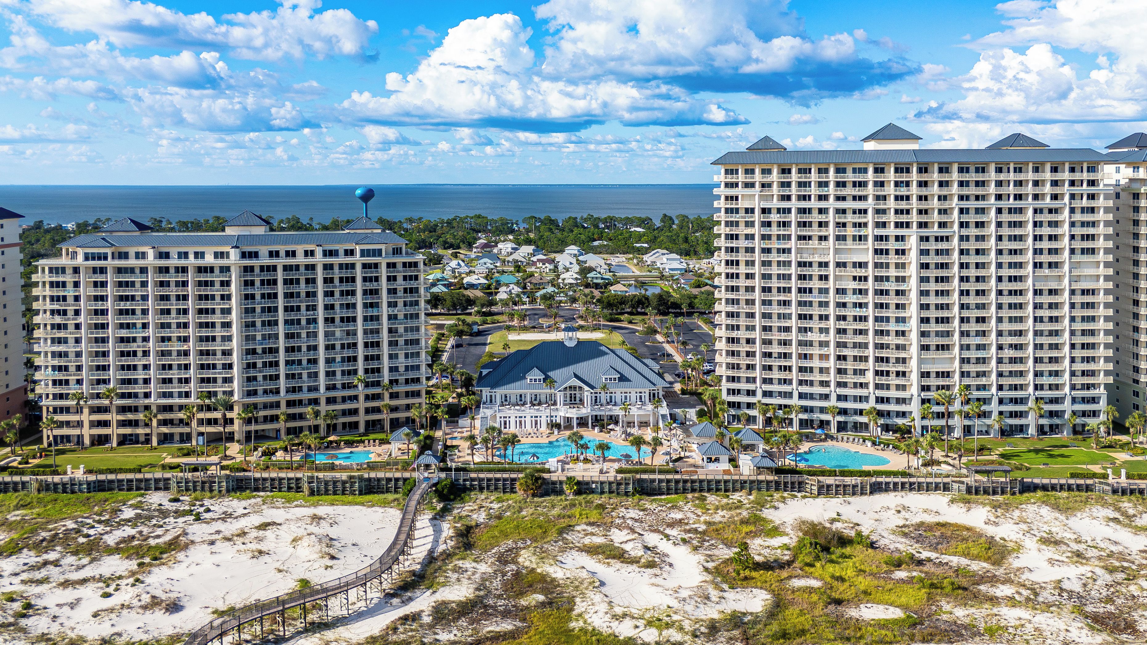 Un resort con varios edificios altos, un área de piscina central y una playa en primer plano.