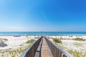 A wooden boardwalk leading to a beach with umbrellas and beachgoers. - Beautiful Resort Condo On The Beach- The perfect getaway (Gulf Shores)